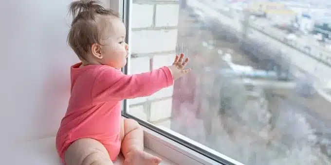 piros ruhás pici baba néz ki az ablakon